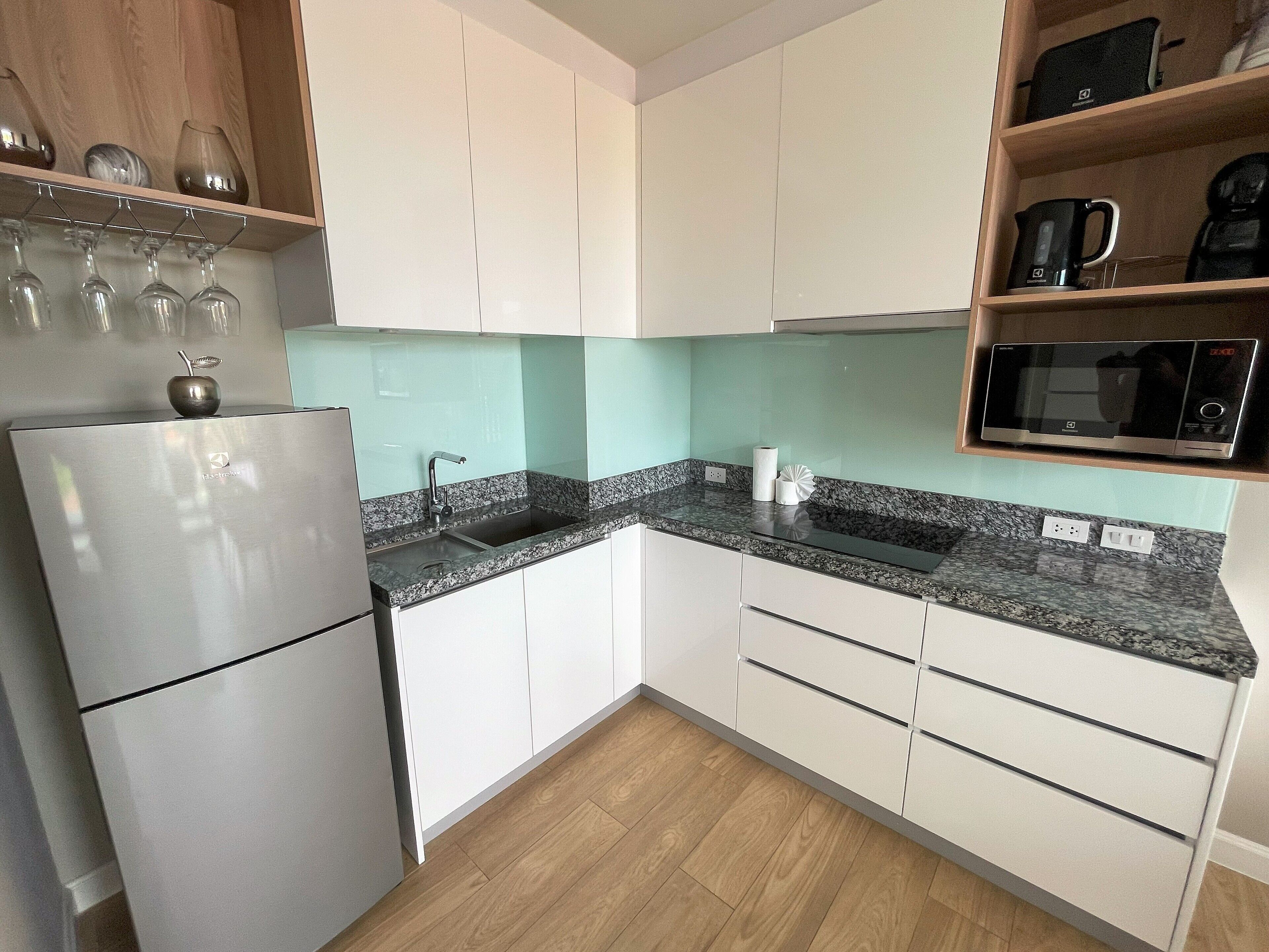 A modern kitchen with white cabinets, a granite countertop, a built-in microwave, and a stainless steel refrigerator.