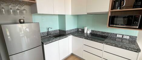 A modern kitchen with white cabinets, a granite countertop, a built-in microwave, and a stainless steel refrigerator.