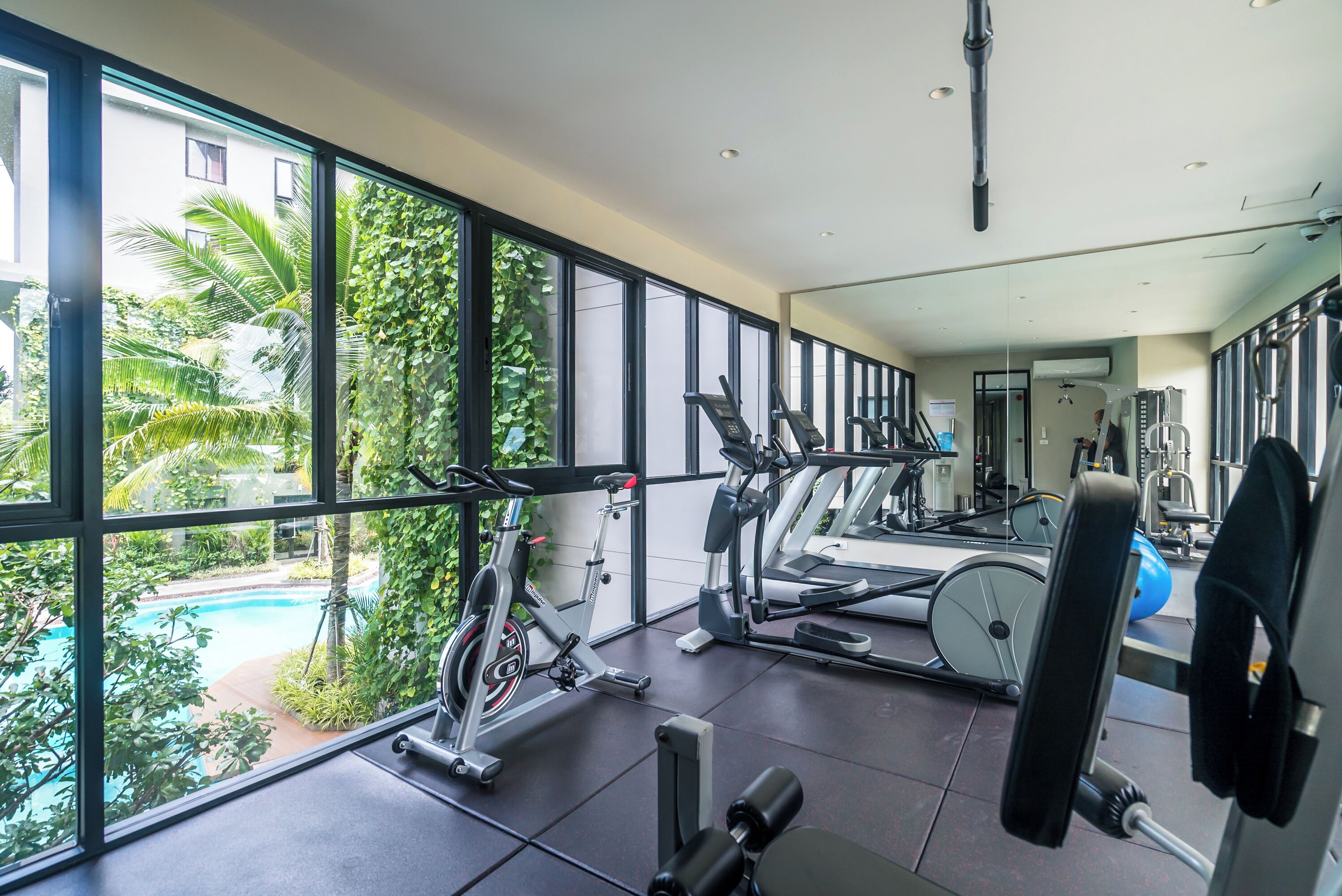 A gym with exercise equipment, large windows, and a view of a swimming pool.