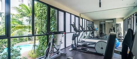 A gym with exercise equipment, large windows, and a view of a swimming pool.