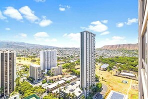 A high-rise building with multiple floors, surrounded by greenery and other buildings. - Waikiki Sunset 28F w/ pool, views & beach walk (Honolulu)