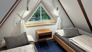 Et lille, trekantet rum med et vindue, en seng, et trænatbord og et skrivebord.