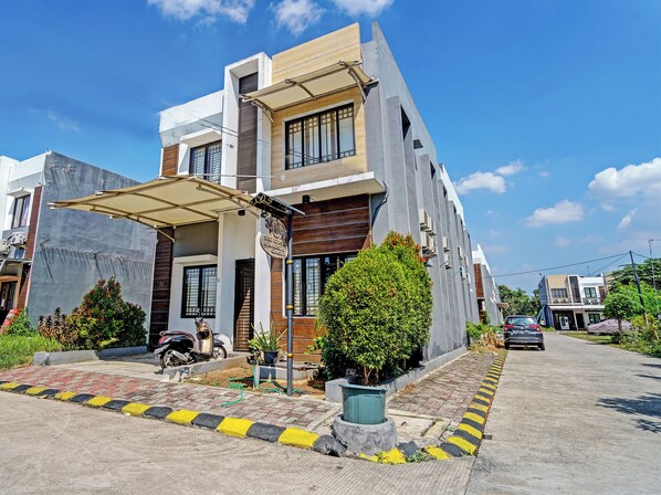 A modern two-story residential building with a flat roof, large windows, and a covered driveway.