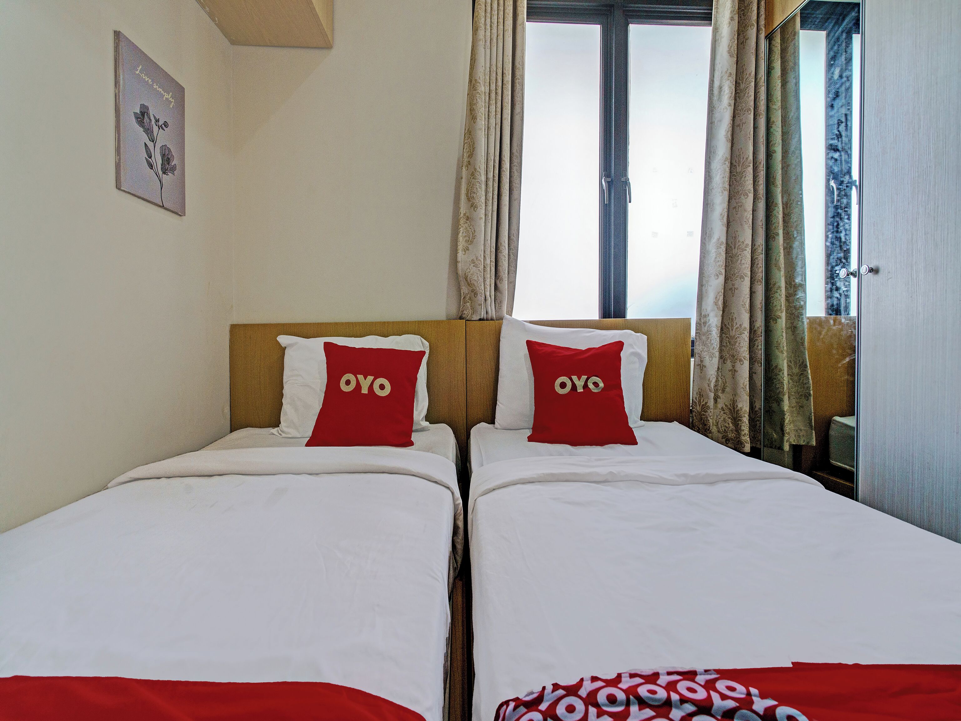 A hotel room with two single beds, each with a red pillow featuring the word "OYO".