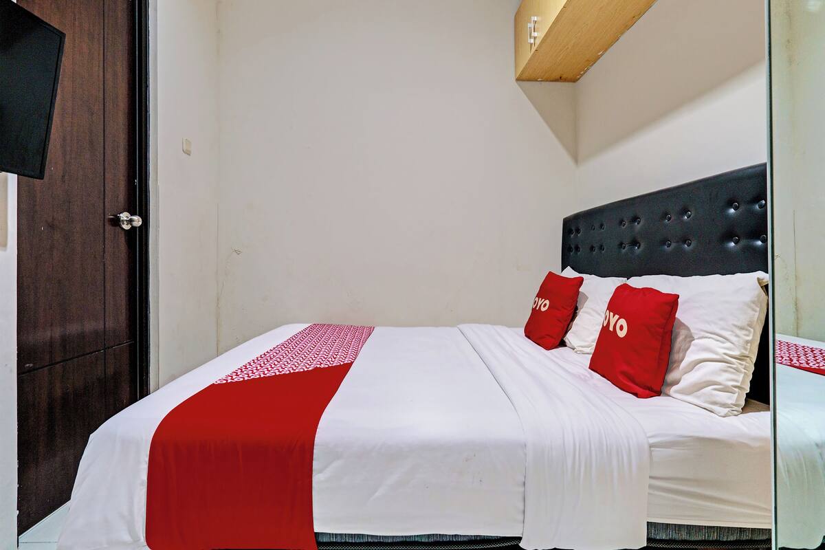A neatly made bed with a white and red bedspread, two red pillows, and a dark headboard.
