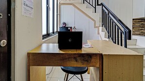 A room with a wooden desk, a laptop, a chair, a staircase with a black railing, and a window with a view of the outside. - OYO 92768 Flagship Exclusive Colombus Near Stasiun Karawang (Karawang)