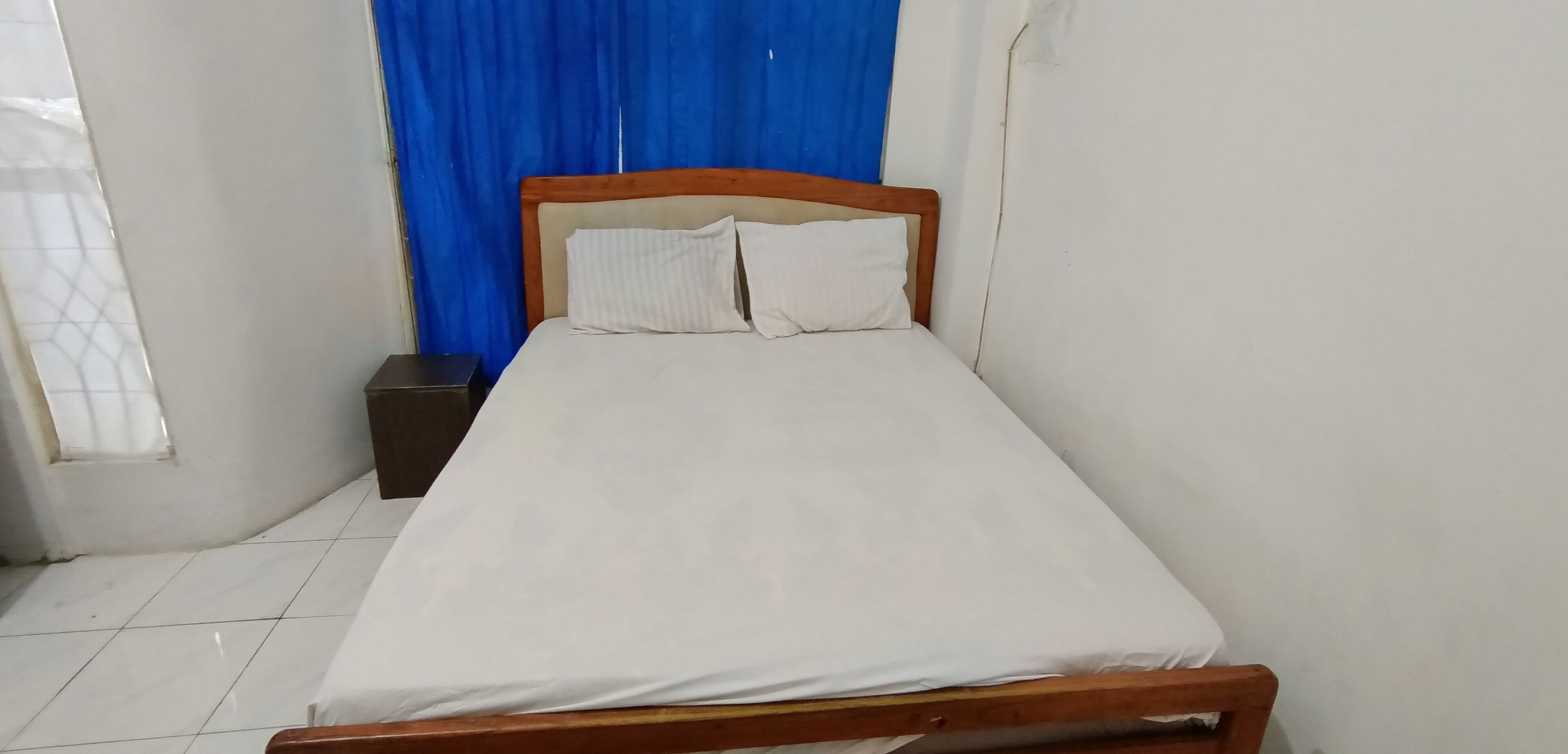 Een eenpersoonskamer met een houten hoofdeinde, wit beddengoed en een klein nachtkastje.