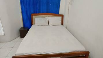 Einzimmer mit einem Einzelbett, Holzkopfstütze, weißer Bettwäsche und einem kleinen Nachttisch.