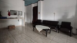 Uma sala de estar com um sofá preto, uma mesa de centro, um espelho e um tecido vermelho pendurado na parede.