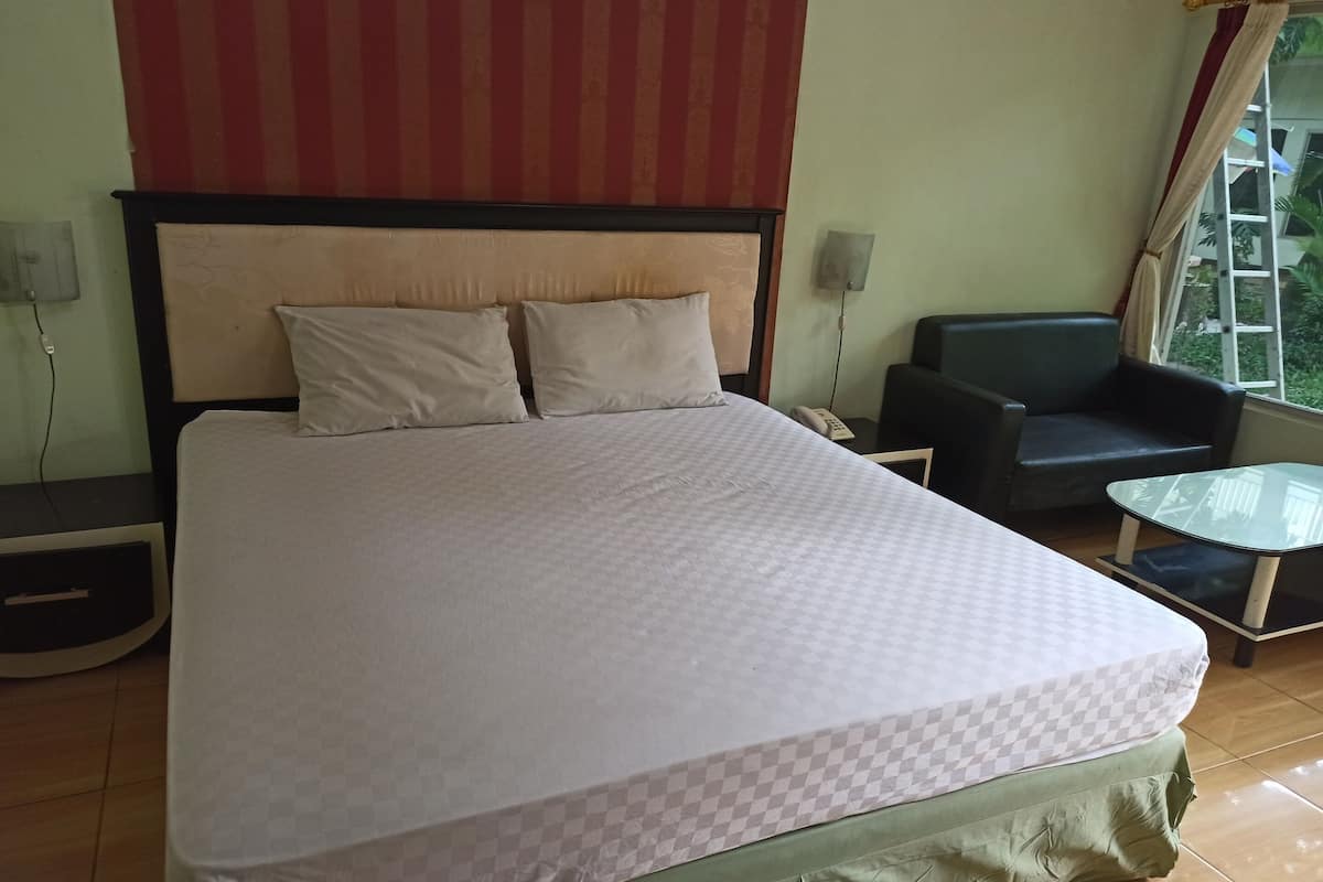 Ein Hotelzimmer mit einem großen Bett, einem Sessel, einem kleinen Tisch und einem Fenster mit Vorhängen.