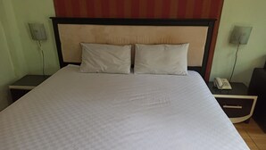 Cama bem arrumada com colcha xadrez e duas almofadas, com mesas de cabeceira de cada lado, com luminárias e telefone.