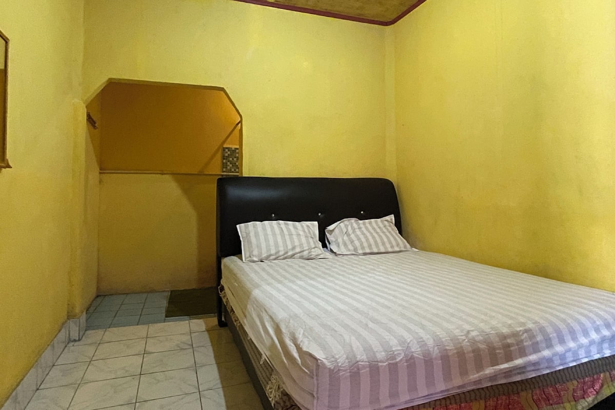 Een kleine kamer met gele wanden, een enkel bed, een tafeltje en een schuin plafond.