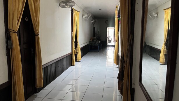 A hallway with white tiled floors, yellow curtains, and ceiling fans. - Hotel O Losmen Griya Mulia Katingan Kuala (Pegatan Hilir)