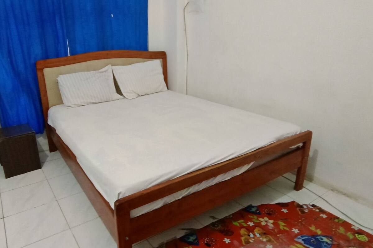 Ein Einzelbett mit Holzrahmen und weißer Bettwäsche in einem Zimmer mit weißen Wänden und einem blauen Vorhang.