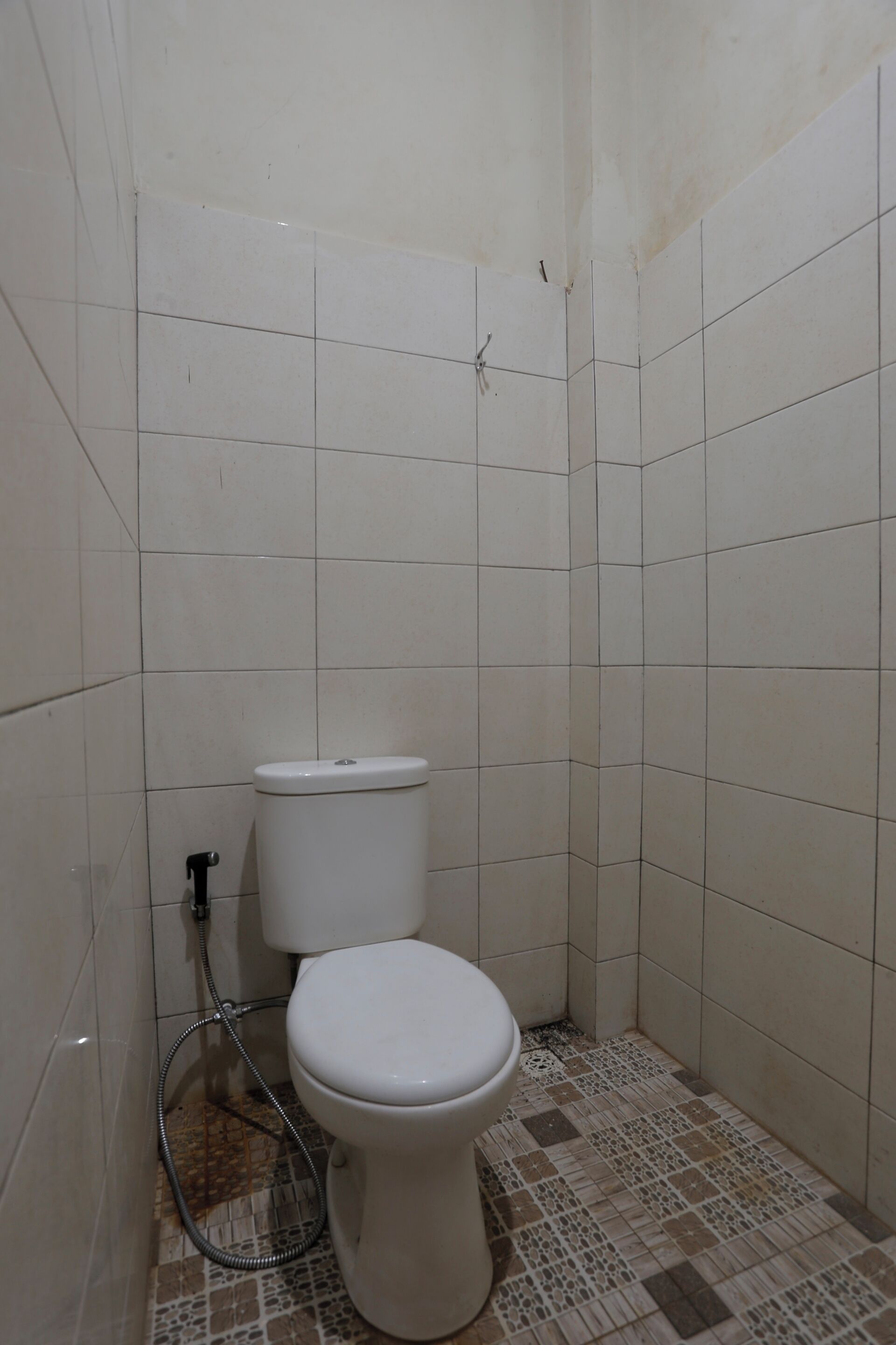 A small, tiled bathroom with a toilet, a shower hose, and a tiled floor.