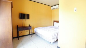 Una habitación con una cama, un escritorio, un televisor montado en la pared y un equipo de aire acondicionado.