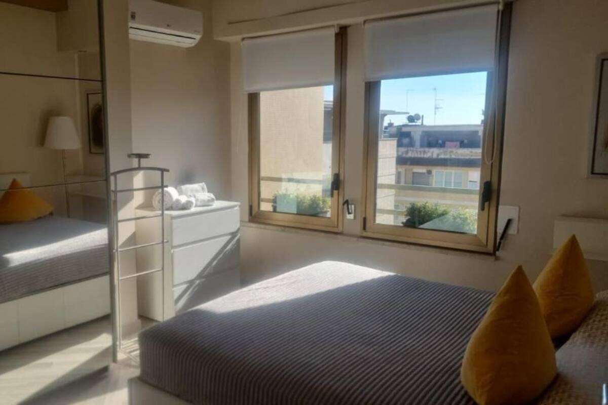 Un dormitorio moderno con cama, un escritorio pequeño, una silla, una ventana con vistas y un balcón.