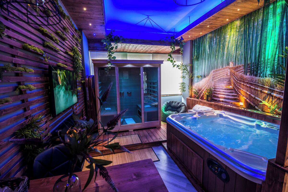 Un moderno espacio de spa con un jacuzzi, suelo de madera y una zona de estar con paredes de cristal.