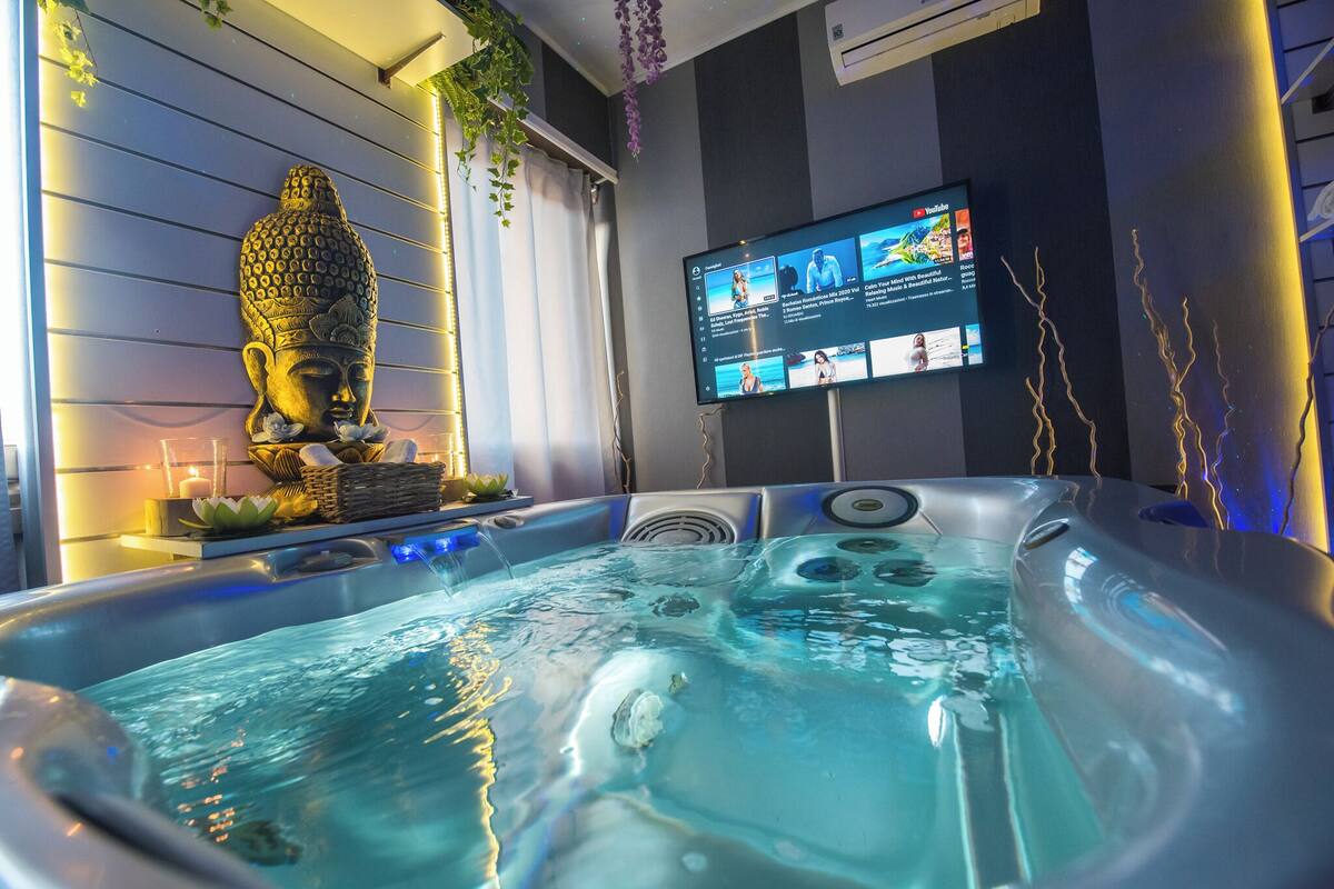 Un jacuzzi con una estatua de Buda, un televisor de pantalla plana y una decoración con flor de loto.