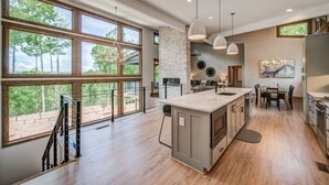 A spacious kitchen with large windows, a central island, and a dining area. - Amazing Grace ~ Indoor Heated Pool ~ Pickleball ~ Basketball ~ Hot Tub ~ Fire Pit (Ellijay)
