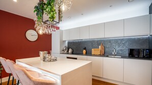 A modern kitchen with white cabinets, a central island with bar stools, a clock on the wall, and a hanging plant with lights. - 3Ten @ Ryedale House -  a premium stay that sleeps 4 guests  in 2 bedrooms (York)