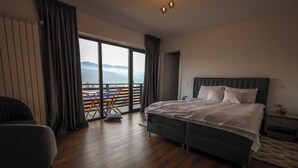 A spacious bedroom with a large bed, a chair, and a view of a mountainous landscape through a sliding door.