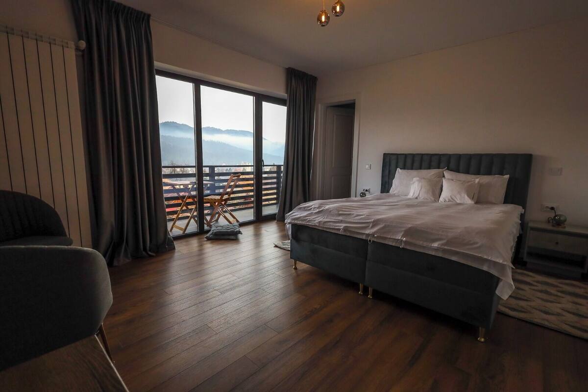 Ein geräumiges Schlafzimmer mit einem großen Bett, einem Sessel und Bergblick durch eine Schiebetür.