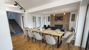 A modern dining area with a wooden table, grey upholstered chairs, a fireplace, and a TV mounted on the wall.