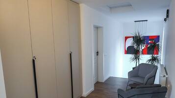 Ein geräumiges Zimmer mit Holzboden, einem grauen Sessel und einer Deckenleuchte.