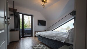A bedroom with a bed, a desk, a chair, a TV, and a view through a window.