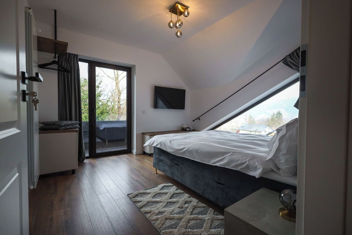 Ein Schlafzimmer mit Bett, Schreibtisch, Stuhl, Fernseher und Blick durch ein Fenster.