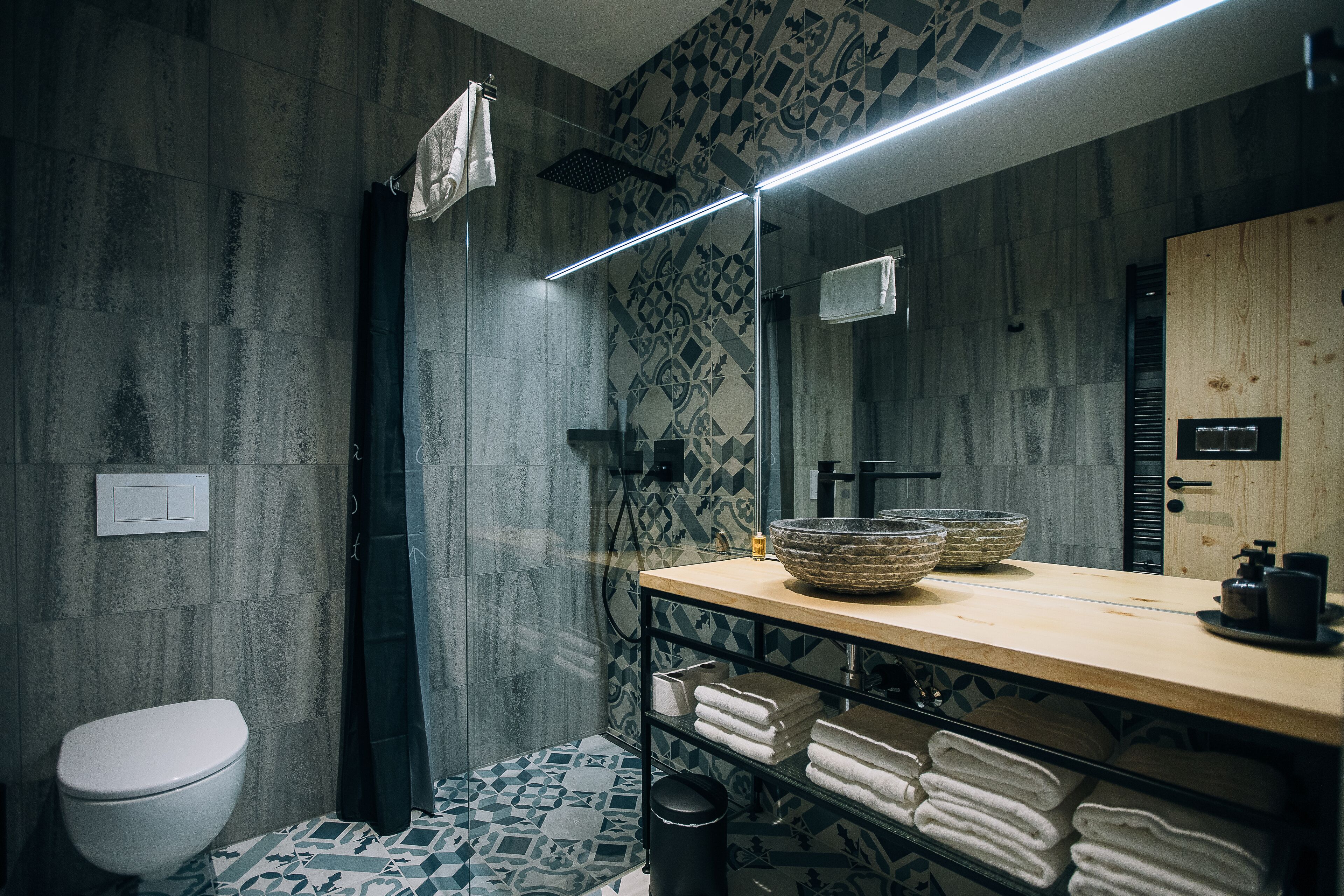 A modern bathroom with a shower, a toilet, a sink with a wooden countertop, and a mirror.