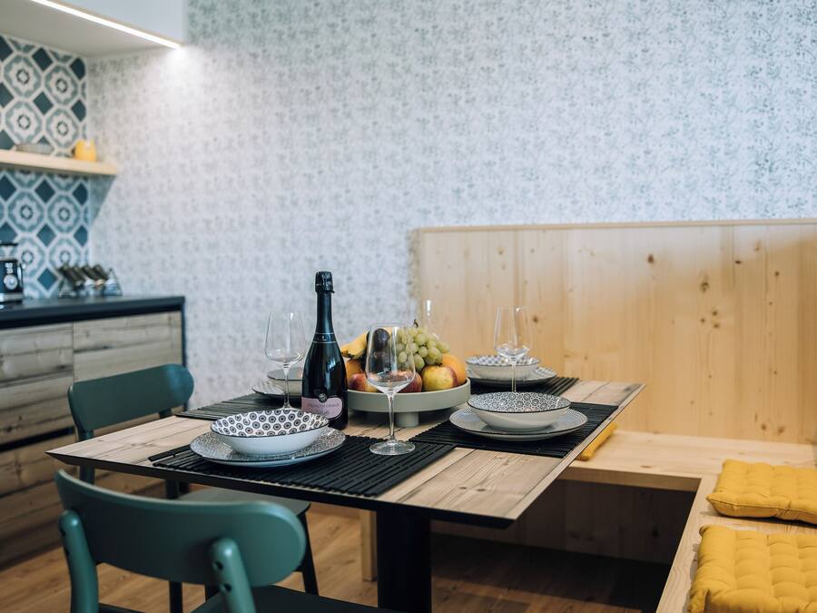 Un comedor con una mesa de madera dispuesta para dos, una botella de vino y un cuenco de fruta.