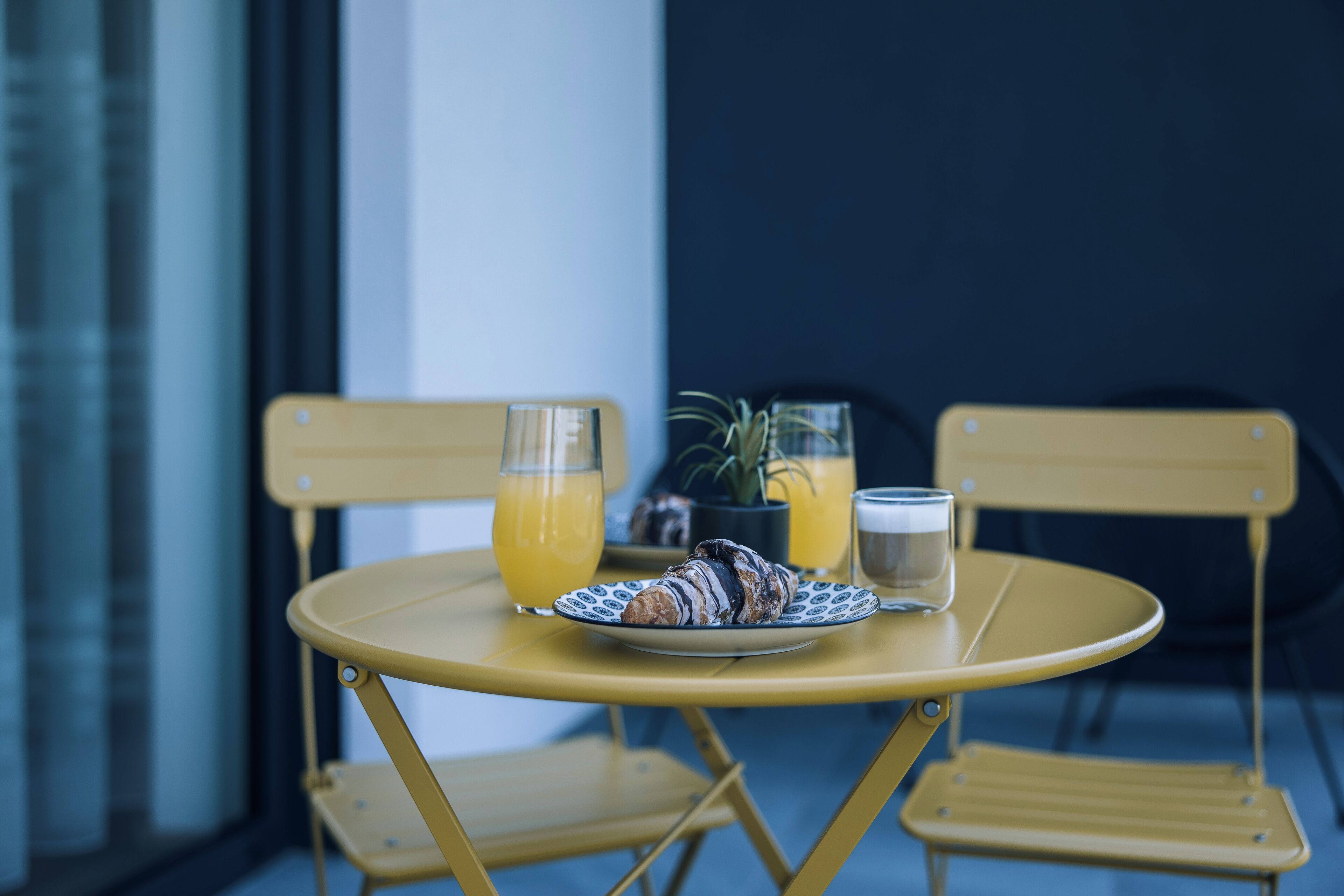 Uma mesa amarela com um prato de croissants e um copo de sumo de laranja.