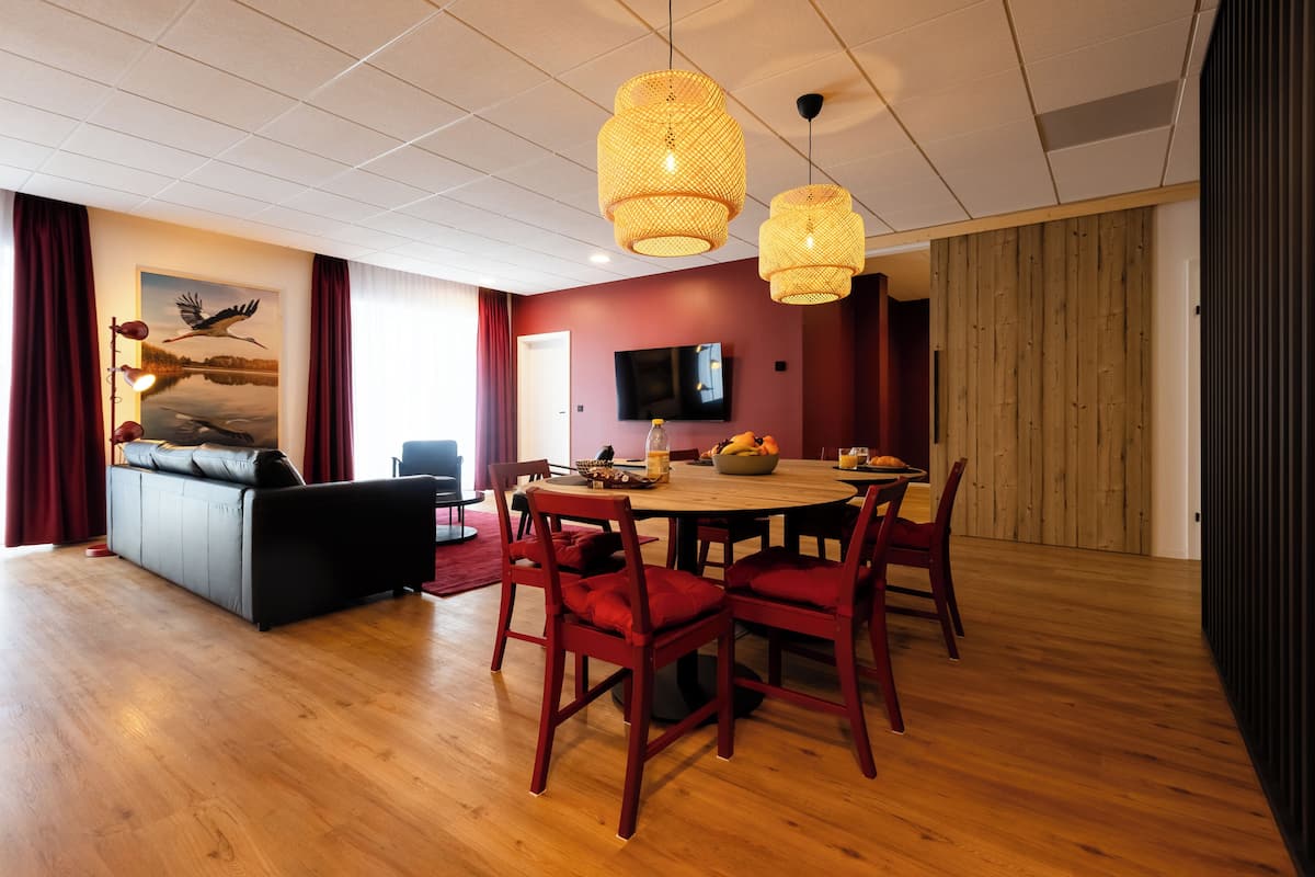 A modern living room with a dining area, wooden flooring, red chairs, a sofa, and a television.