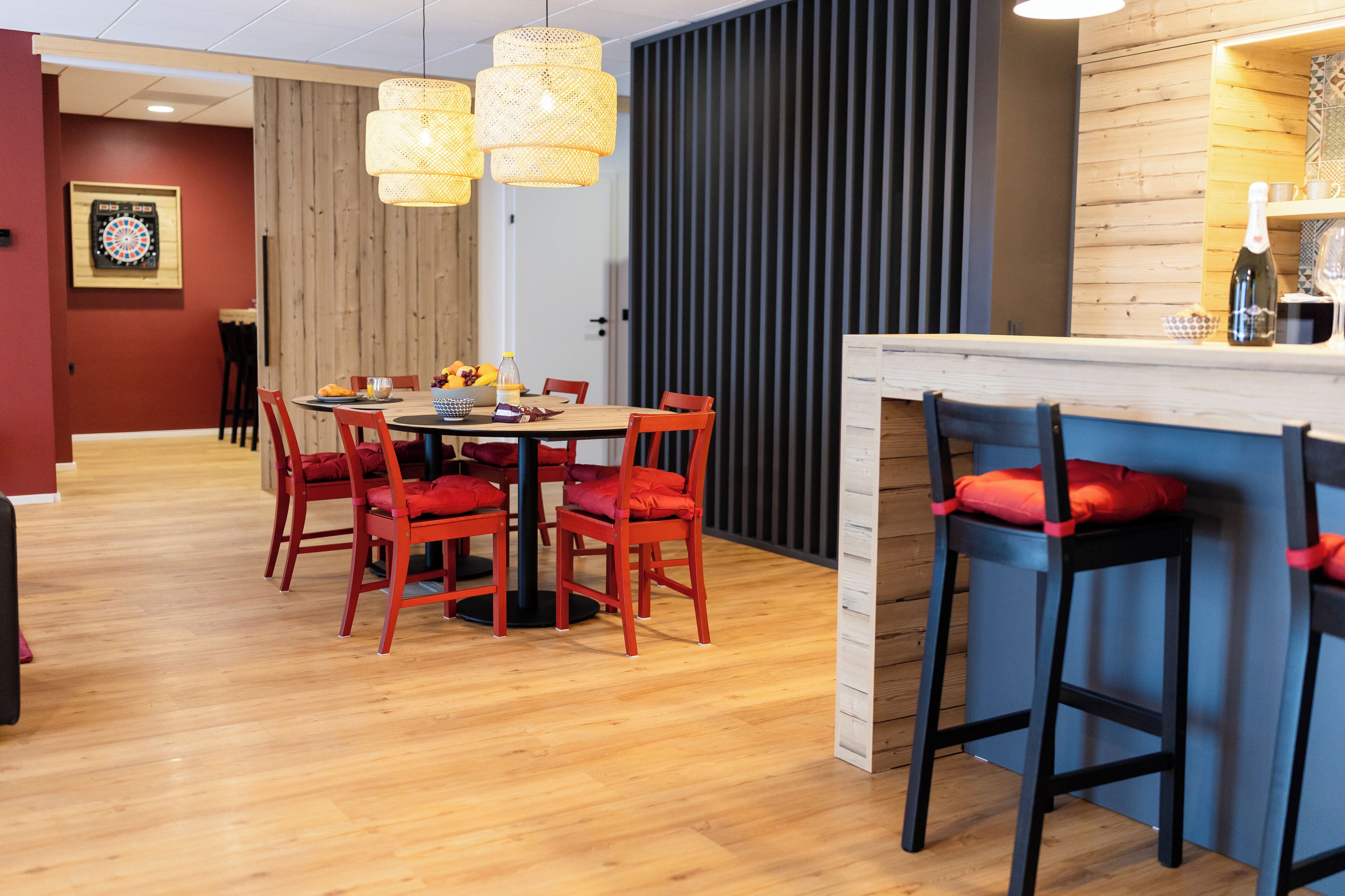 Een eetgedeelte met een houten tafel, rode stoelen en een bar met krukjes.