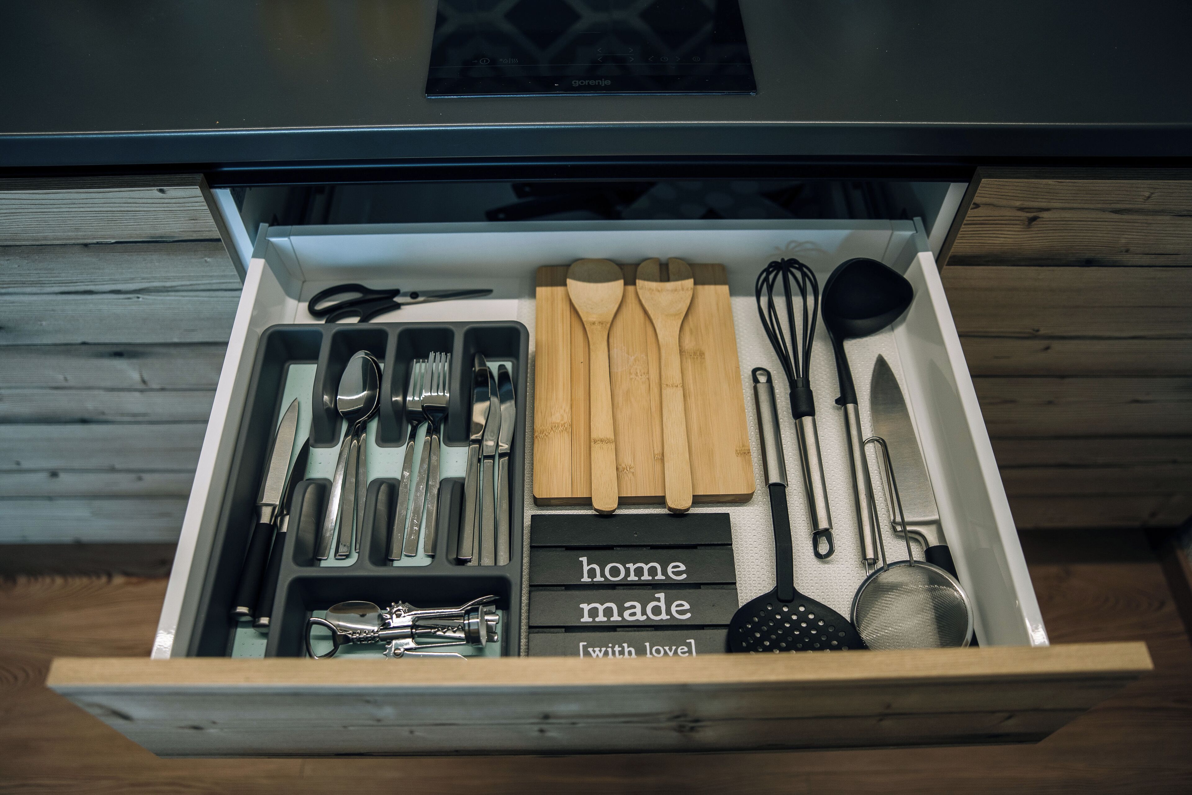 Un cajón de cocina con utensilios, como cuchillos, cucharas y un batidor.