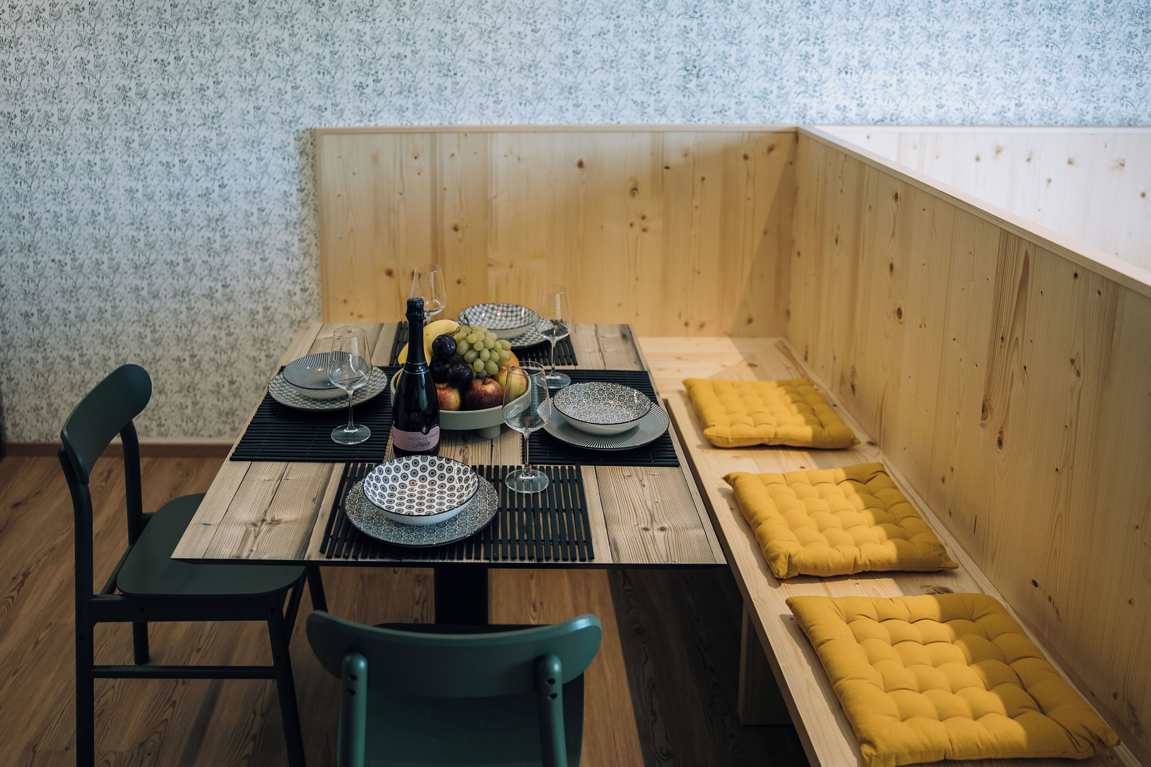 A wooden dining table set with plates, glasses, and a bowl of fruit.