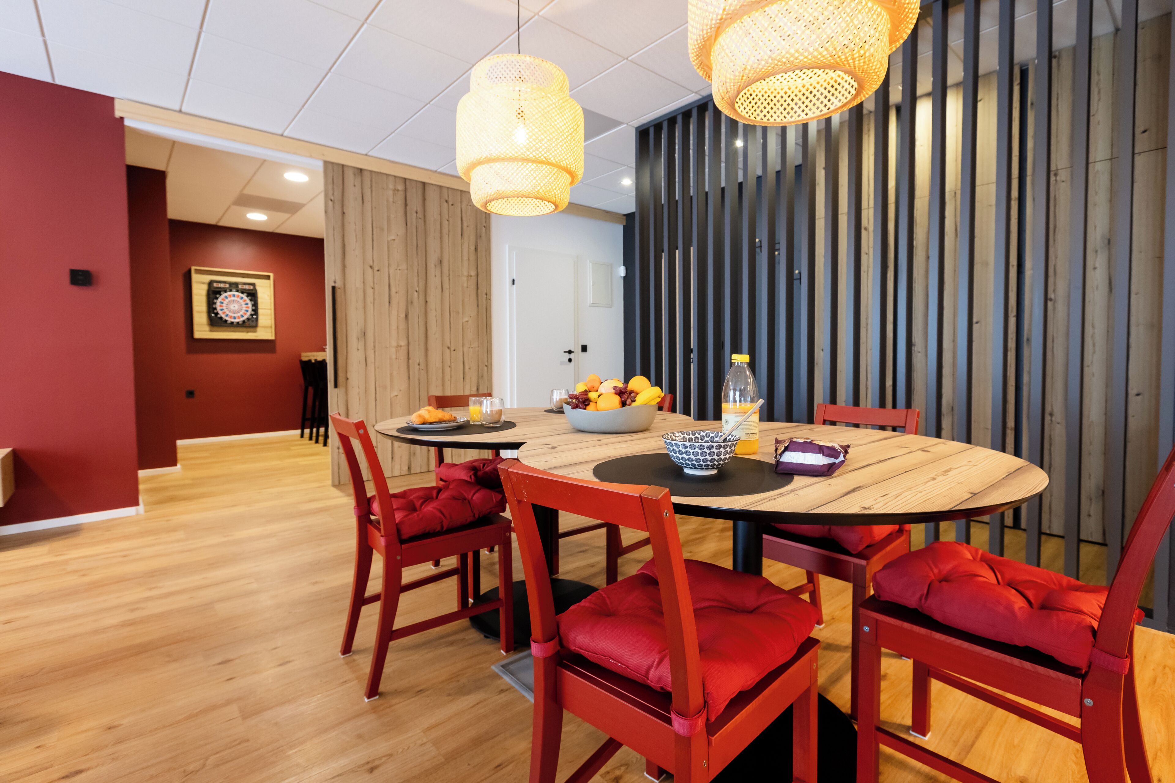 Un comedor con una mesa redonda de madera, sillas tapizadas en rojo y un frutero.