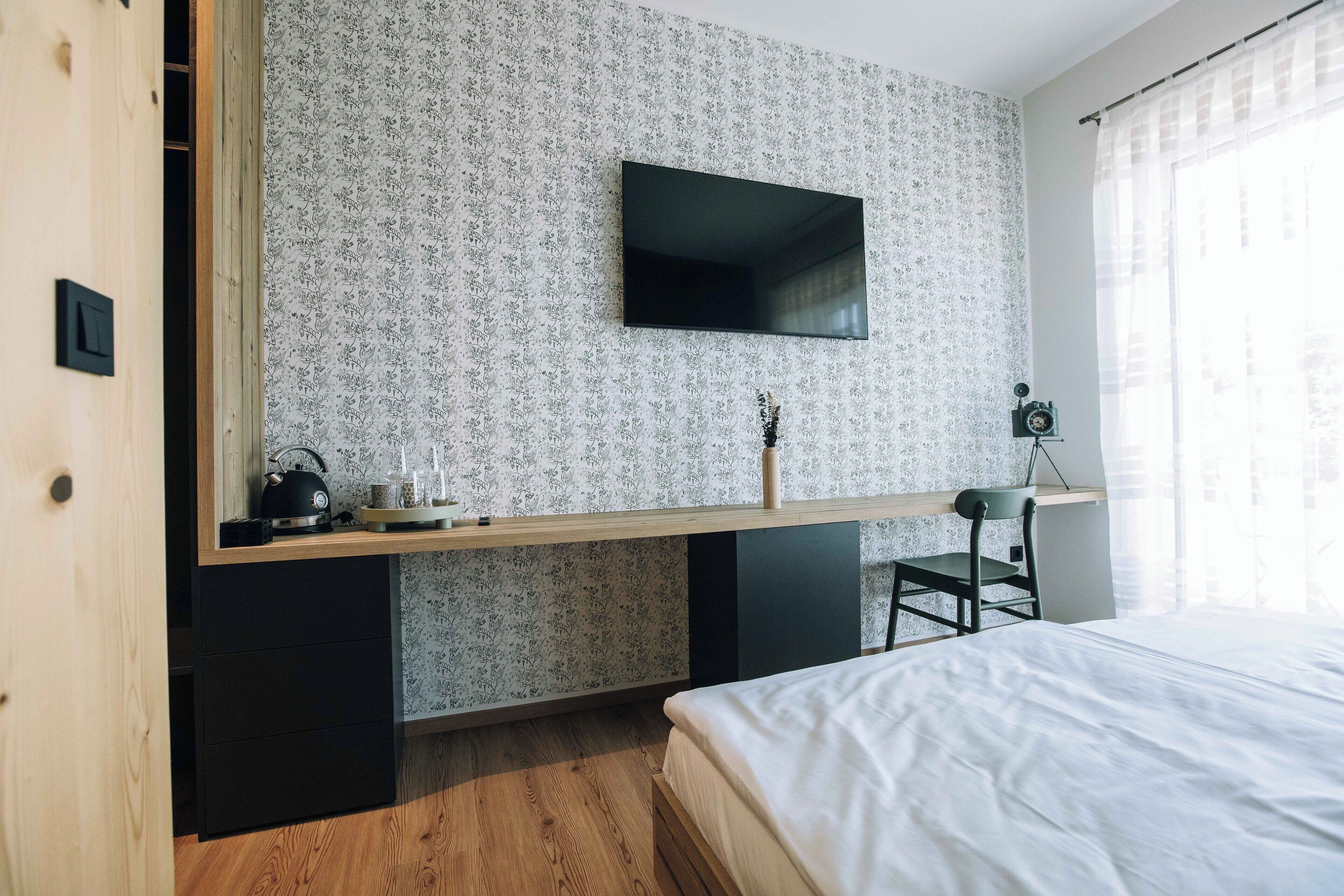 Un dormitorio con una cama, un escritorio con televisor de pantalla plana, una silla y una mesita con hervidor y tazas.