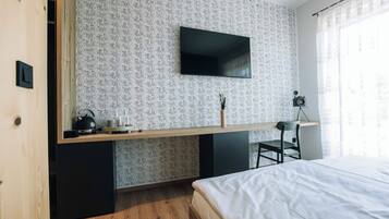 Un dormitorio con una cama, un escritorio con televisor de pantalla plana, una silla y una mesita con hervidor y tazas.