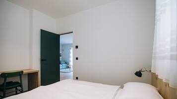 Een slaapkamer met een bed, een bureau en een stoel. Er is een deur die naar een andere kamer leidt.