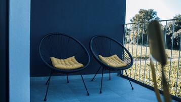 Two black wire-framed chairs with yellow cushions on a balcony with a metal railing, against a dark blue wall.