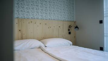 A bedroom with a wooden headboard, two white beds, a wall-mounted lamp, and a floral-patterned wallpaper.