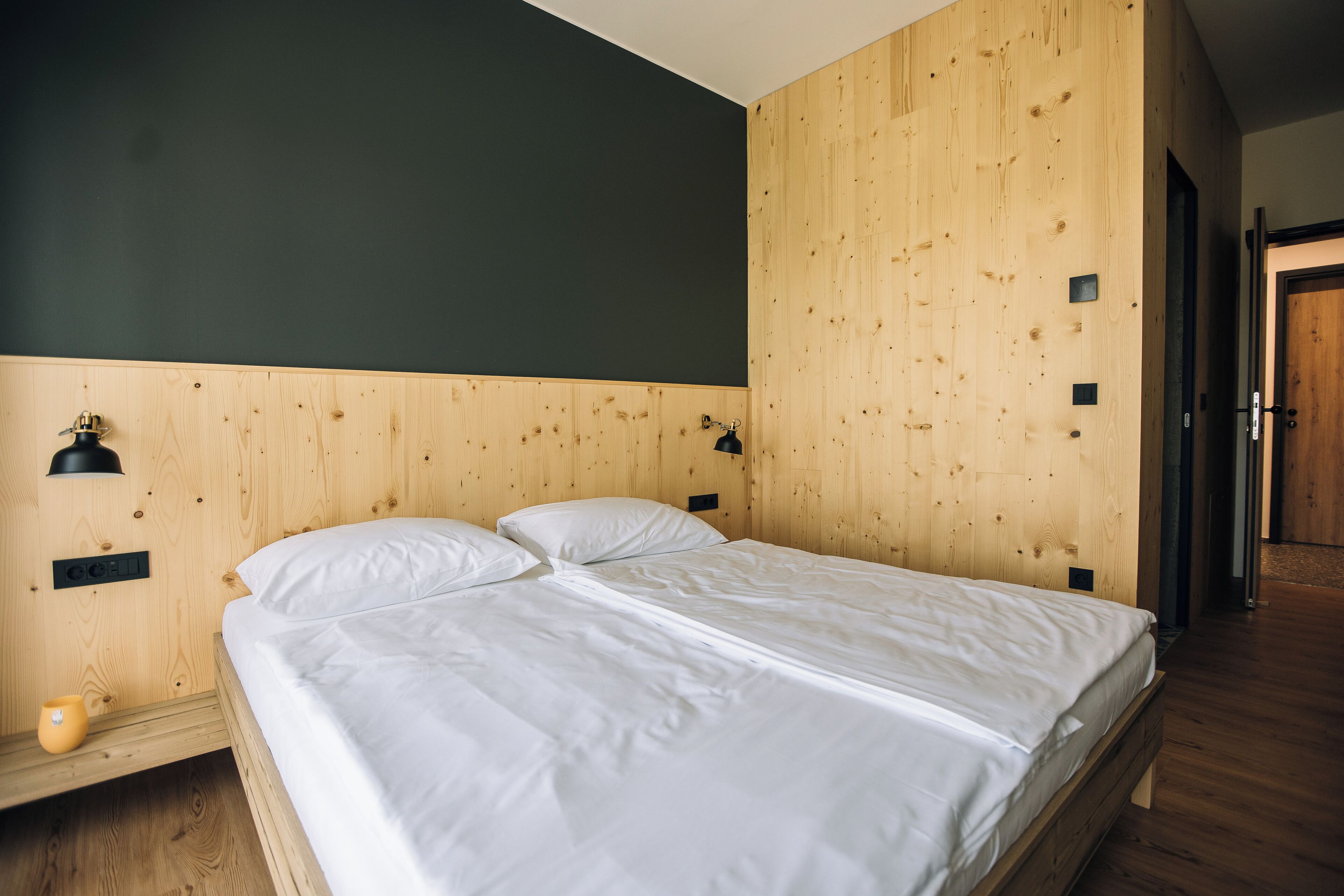 Habitación con paneles de madera, una cama, una mesita de noche y una lámpara fijada a la pared.