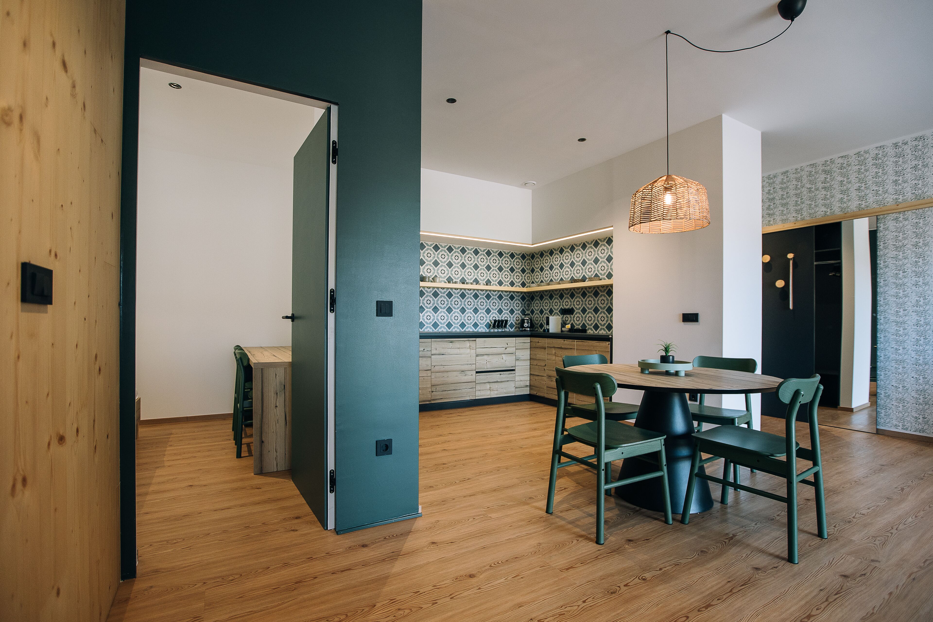 Une cuisine moderne avec une table et des chaises en bois, un luminaire suspendu et des carreaux décoratifs sur le mur derrière l’évier.