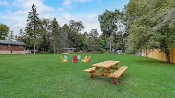 Un patio trasero con una mesa de picnic de madera y sillas Adirondack de colores.