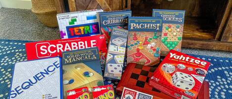 Variedad de juegos de mesa, incluyendo Scrabble, Tetris, Pachisi y otros, dispuestos sobre una alfombra estampada.