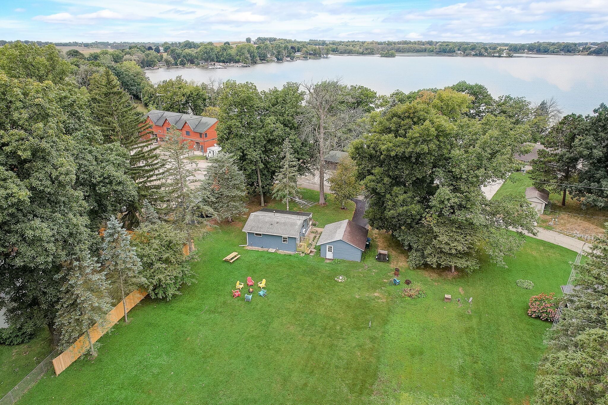 A residential area with a large house, a smaller shed, and a grassy yard with a few chairs.