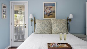 A bedroom with a bed, two bedside lamps, a painting, and a tray with glasses and a plate of food.